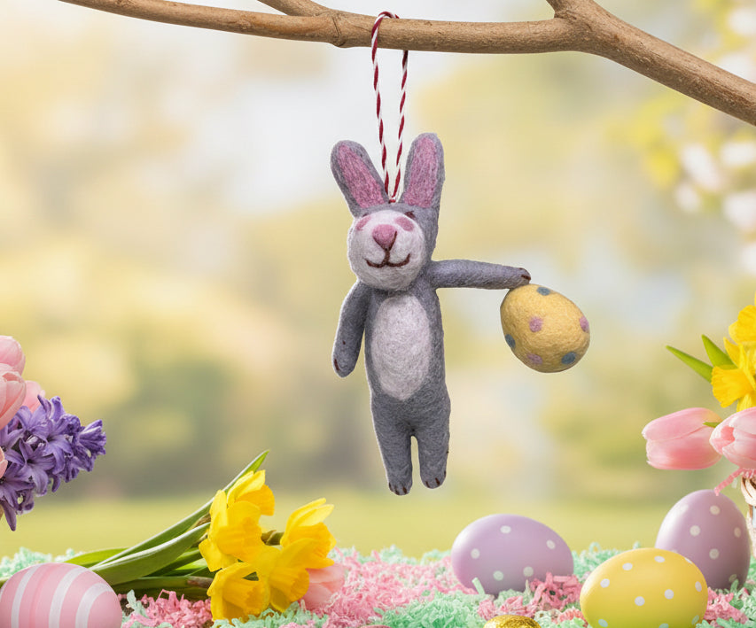 Handmade felted rabbit toy holding a yellow egg on a textured fabric background