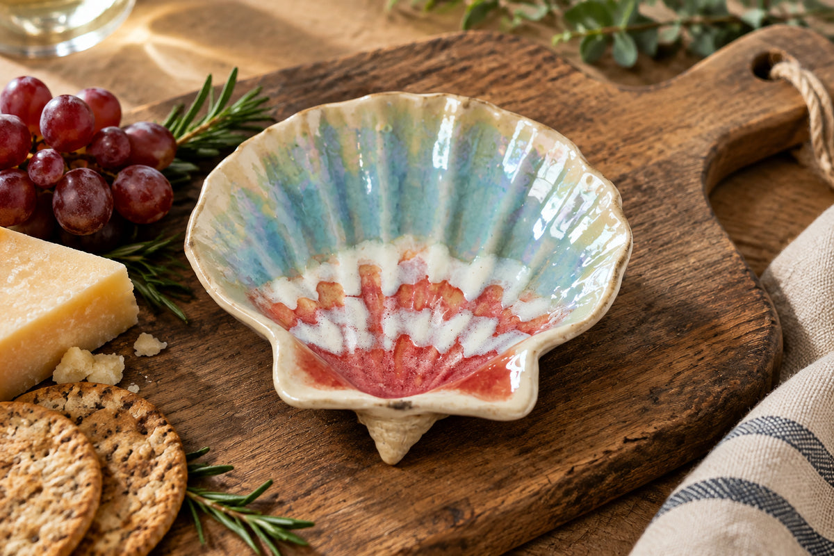 A small shell-shaped dish with a scalloped rim, featuring a beige exterior and a patterned interior with blue, white, and red sections, placed on a white surface.